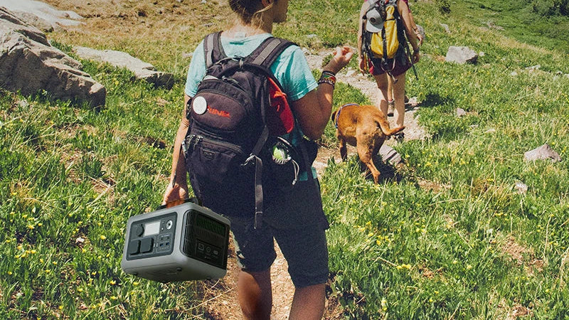 Two people hiking with backpacks on a trail, carrying a 32LB portable device.