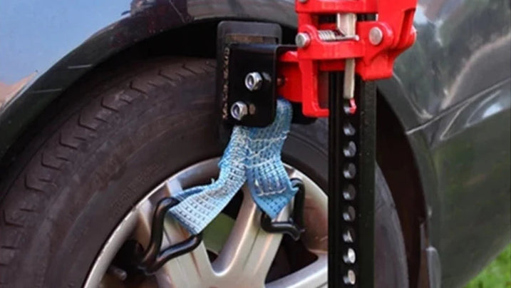 Red car jack with a blue strap attached to a black car tire.