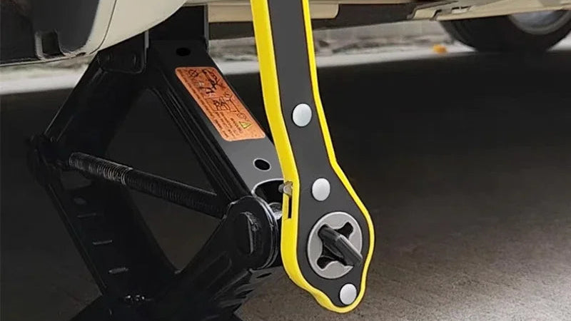Car jack with yellow handle attached to a white car on a concrete floor.