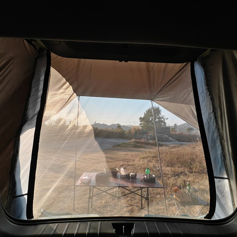 View from inside the Overland Tailgate Tent through its mesh window looking out at a camp table and mountain scenery