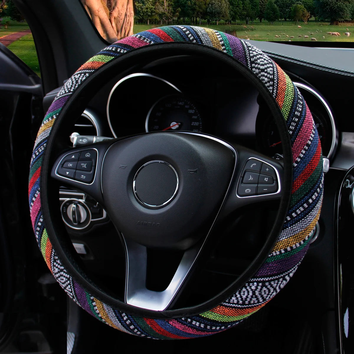 Multicolour striped bohemian linen steering wheel cover fitted on a car steering wheel viewed against a green outdoor background