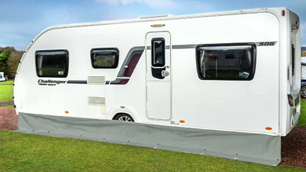 A white Challenger caravan parked on green grass under a blue sky with clouds. The caravan has dark tinted windows, a gray undercarriage, and visible Challenger branding on the side.