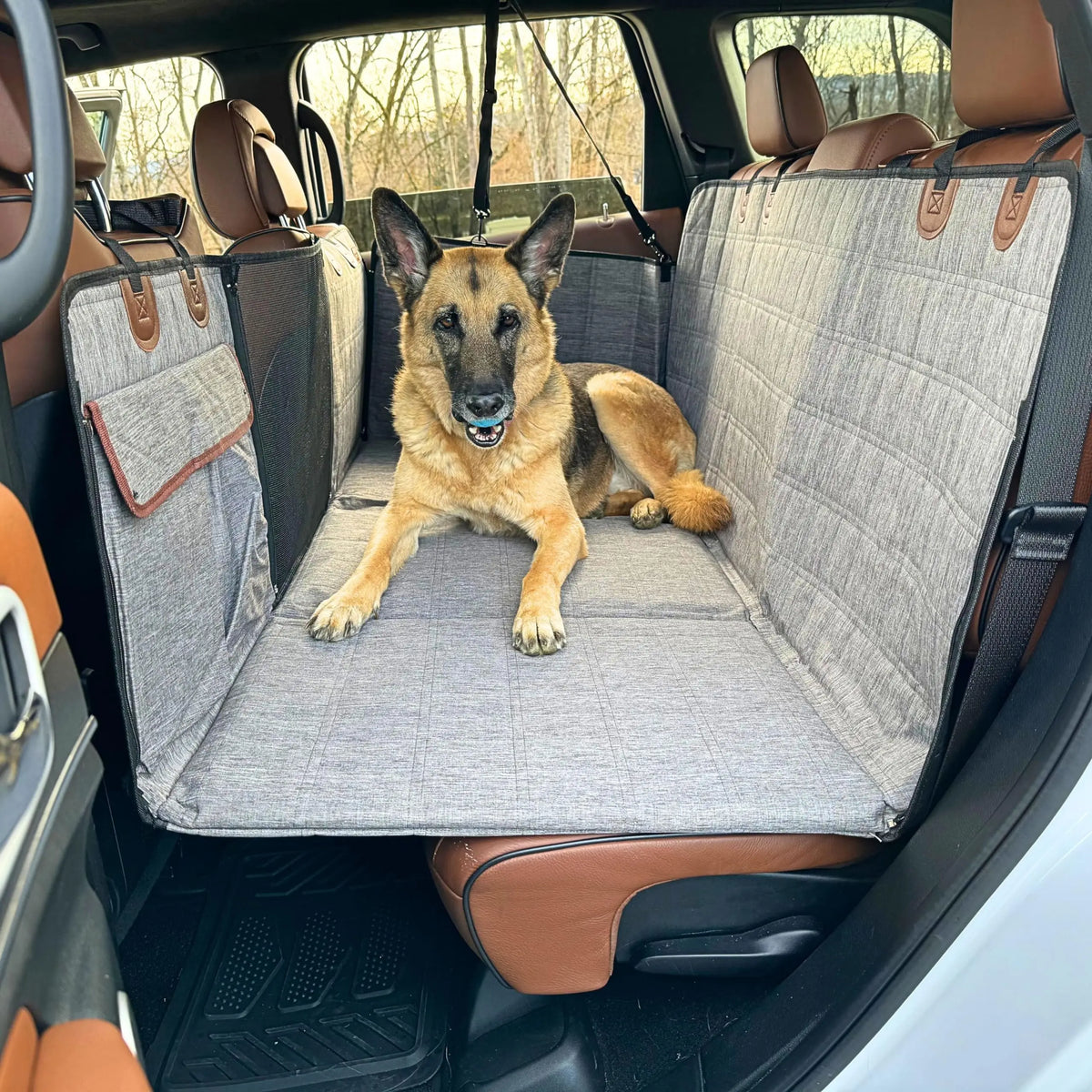 Hard-Base Dog Seat Extender in grey installed in an SUV back seat, German Shepherd lying on the flat platform with headrest straps fitted