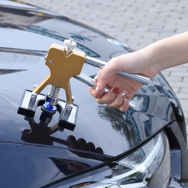 Hand using a Paintless Dent Repair suction cup dent puller with glue tab attached to lift a dent from a black car body panel outdoors.