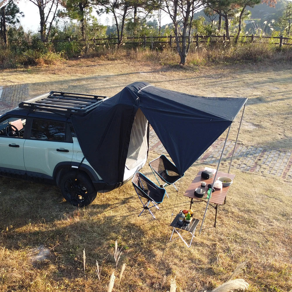 Overland Tailgate Tent deployed off a white SUV in a grassy field with camp chairs and a table for outdoor dining