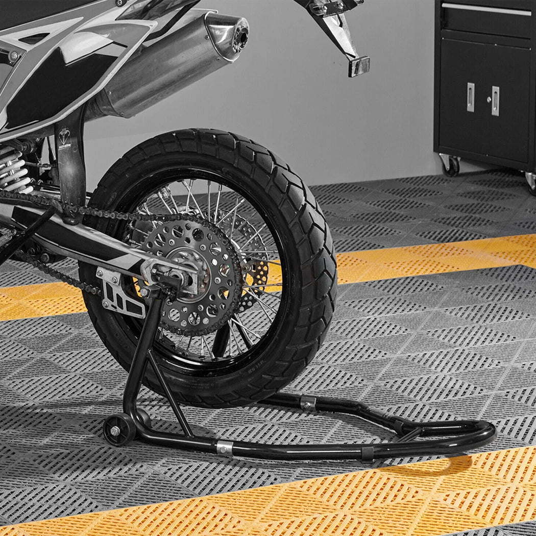 Black and white photo of a motorcycle rear wheel raised on a Heavy-Duty Paddock Stand with a yellow floor marking