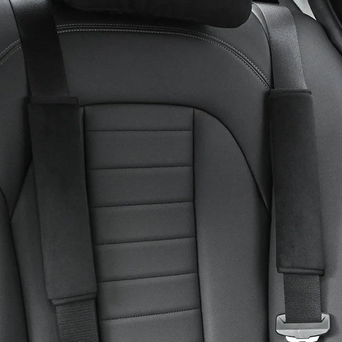 Black seat belt shoulder covers fitted to both front seat belts in a car with grey leather upholstery