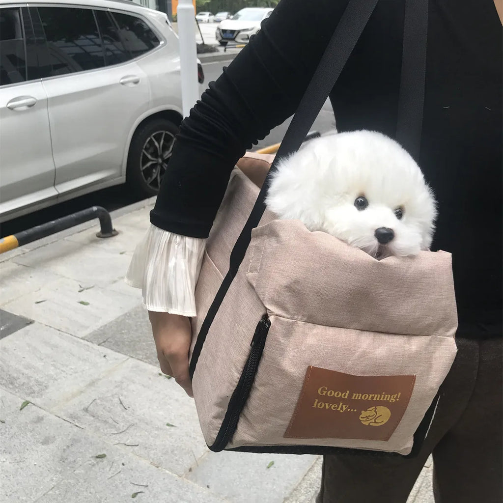 Beige console pet booster seat carried as a shoulder bag outdoors, with a white fluffy dog peeking out