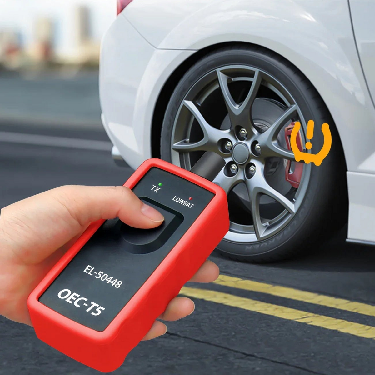 Hand holding GM TPMS relearn tool beside a car tyre to reset the tyre pressure warning light