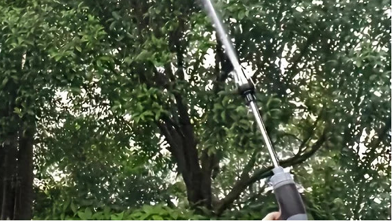 Hose nozzle spraying water into the air with trees in the background