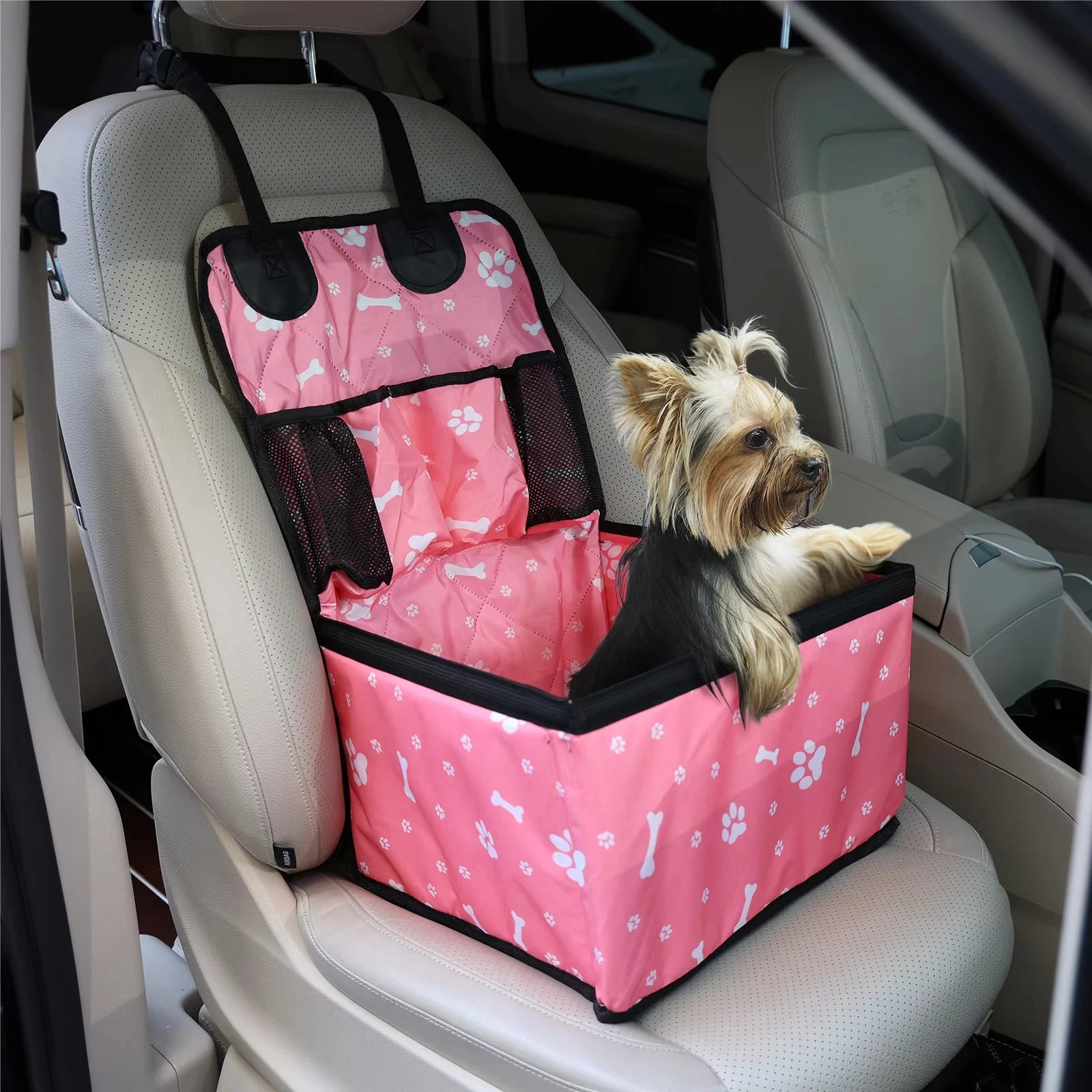 Yorkshire terrier sitting inside a pink paw print waterproof dog car booster seat on the front passenger seat