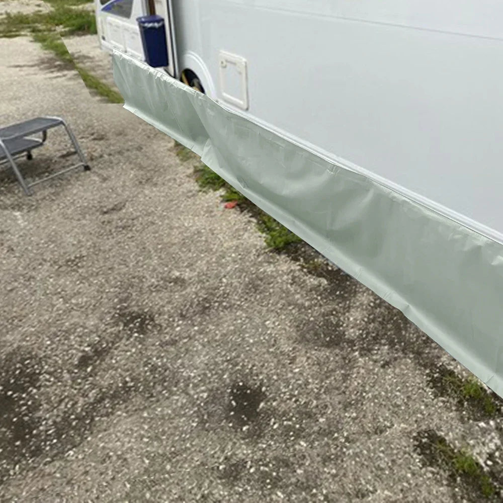 Caravan Awning Draught Skirt running along the side of a white caravan on a gravel campsite, closing the gap under the chassis