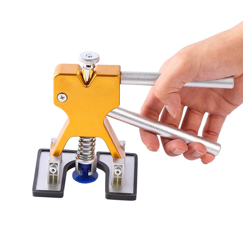 Hand gripping the gold-tone dent puller tool from the Paintless Dent Repair Kit, showing the blue glue tab attachment on a white background.