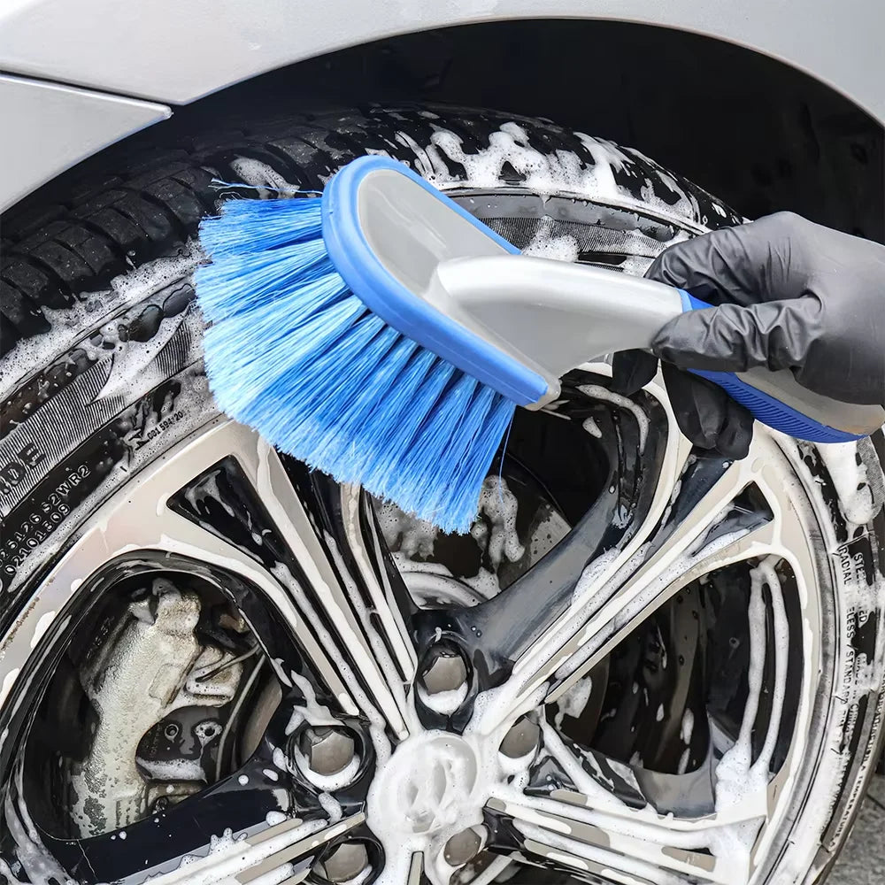 Gloved hand scrubbing a soapy car tyre sidewall with a blue bristle detailing brush