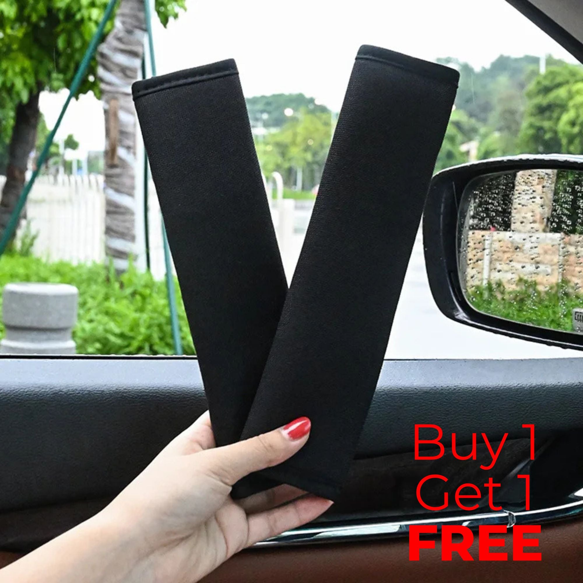Hand holding two black seat belt shoulder covers inside a car with Buy 1 Get 1 Free offer shown