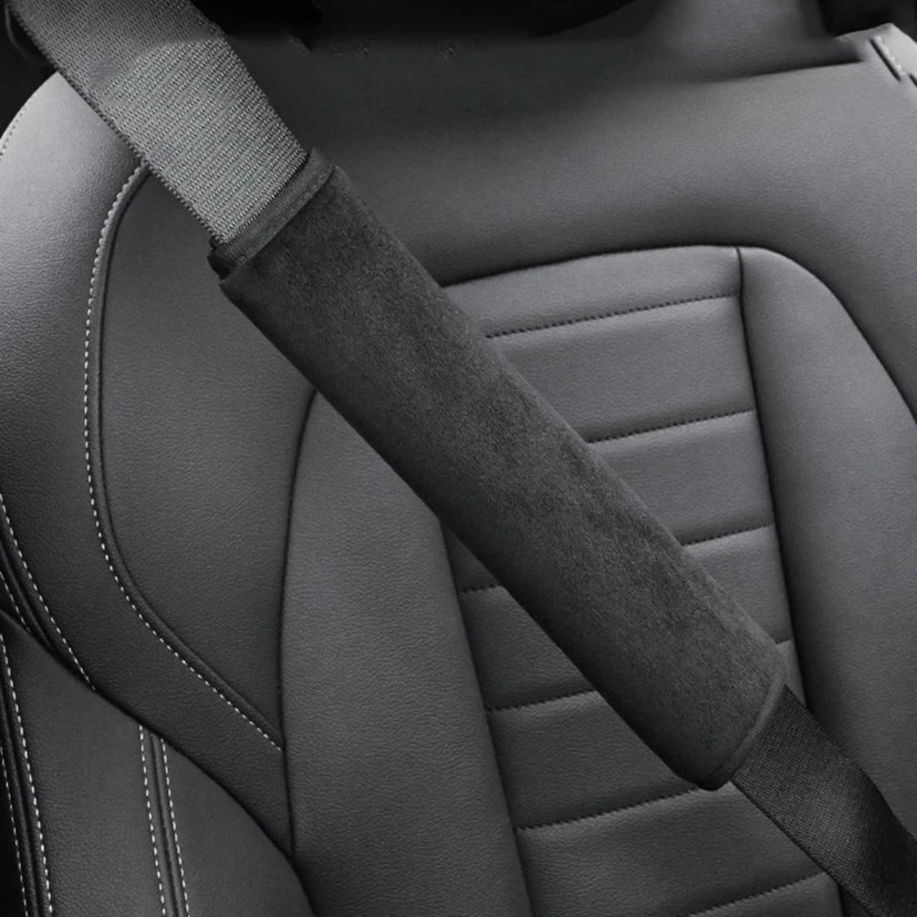 Black seat belt shoulder cover fitted over a seat belt strap against a grey leather car seat, close-up