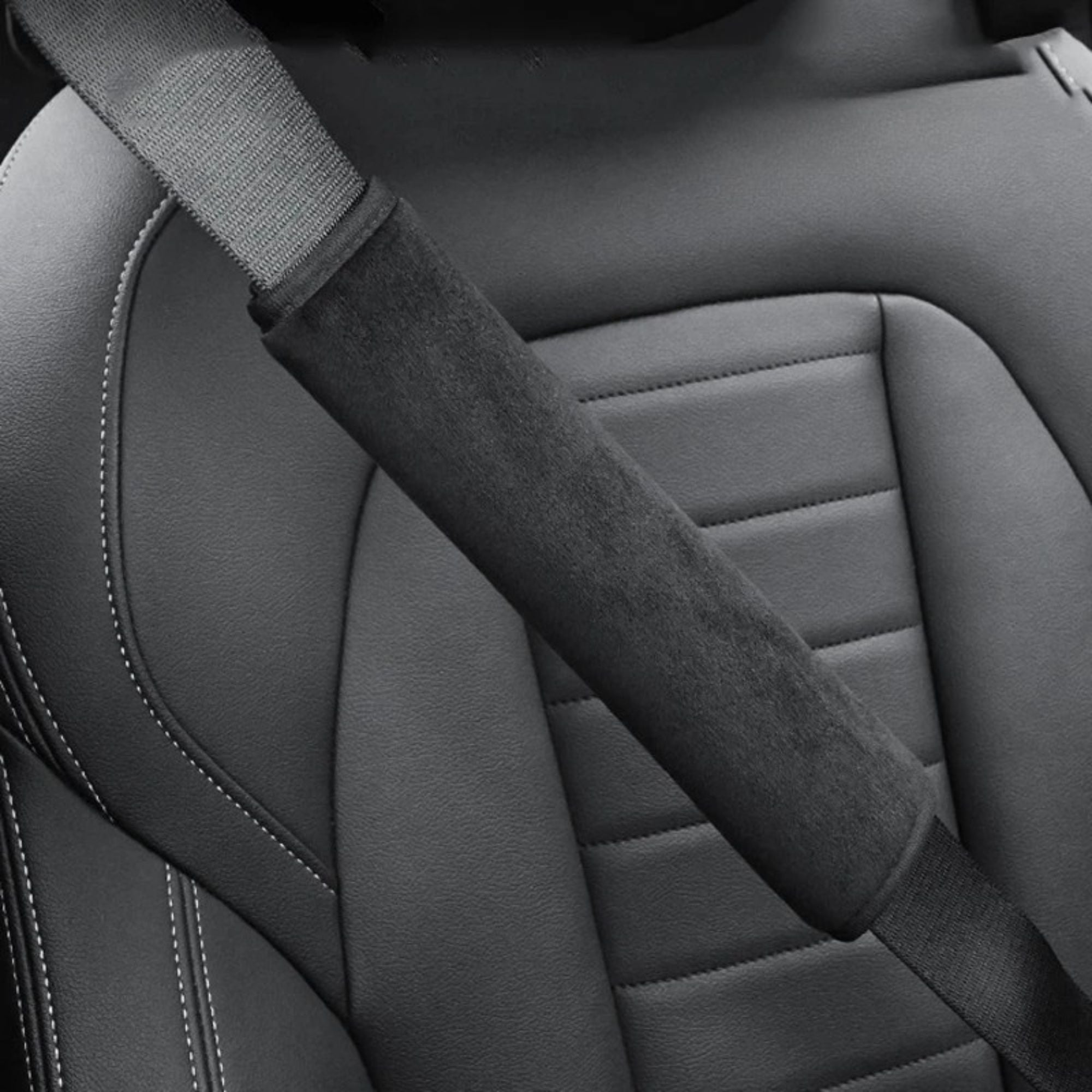 Black seat belt shoulder cover fitted over a seat belt strap against a grey leather car seat, close-up