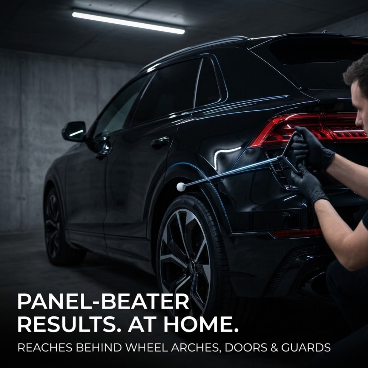 Person in black gloves using the Dent Removal Rod Kit behind the rear wheel arch of a black SUV in a garage