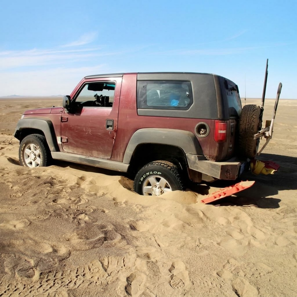 Red 4WD bogged in desert sand with a red Heavy-Duty Recovery Track wedged under the rear tyre