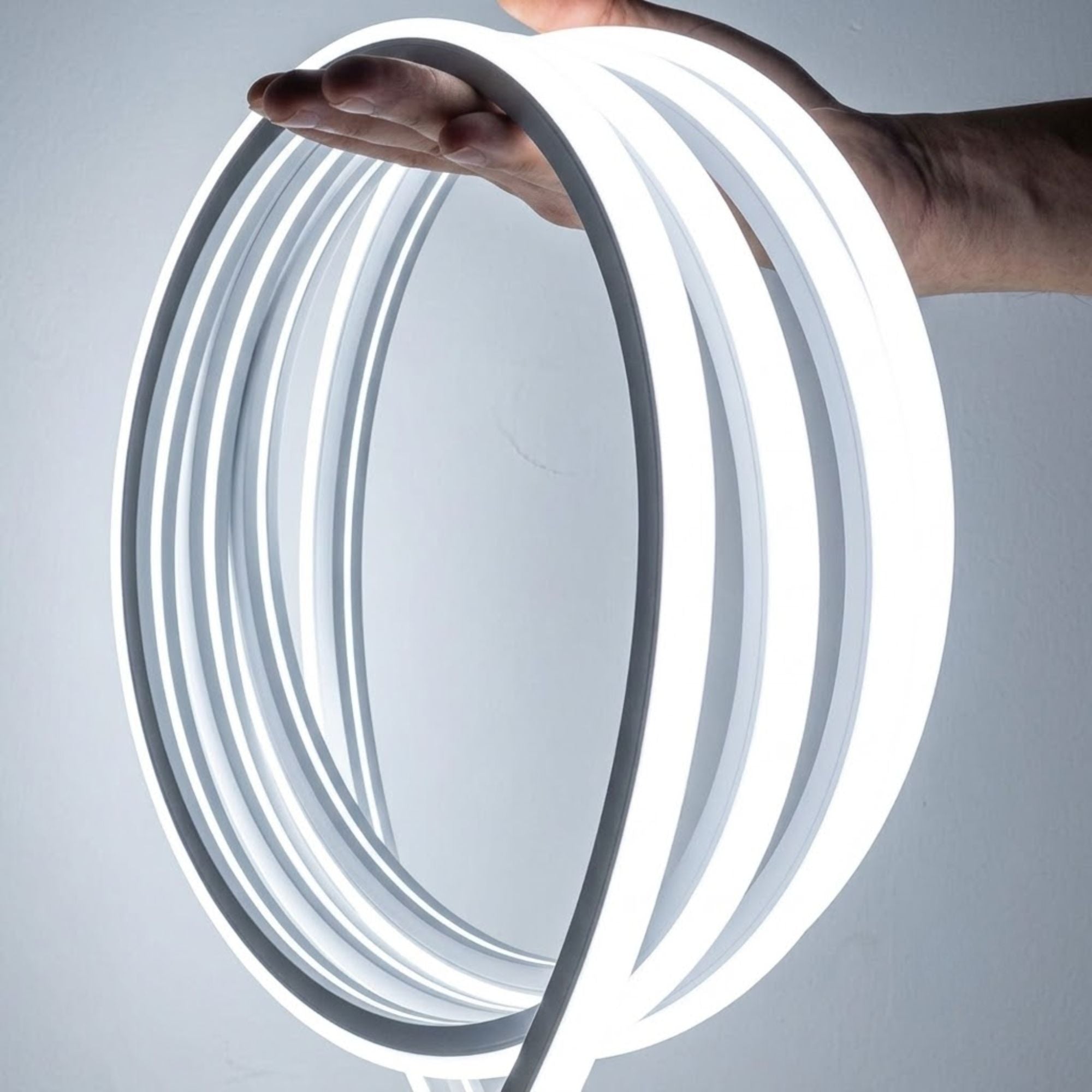 Hand holding a coiled flexible LED trunk light strip glowing bright white against a plain background