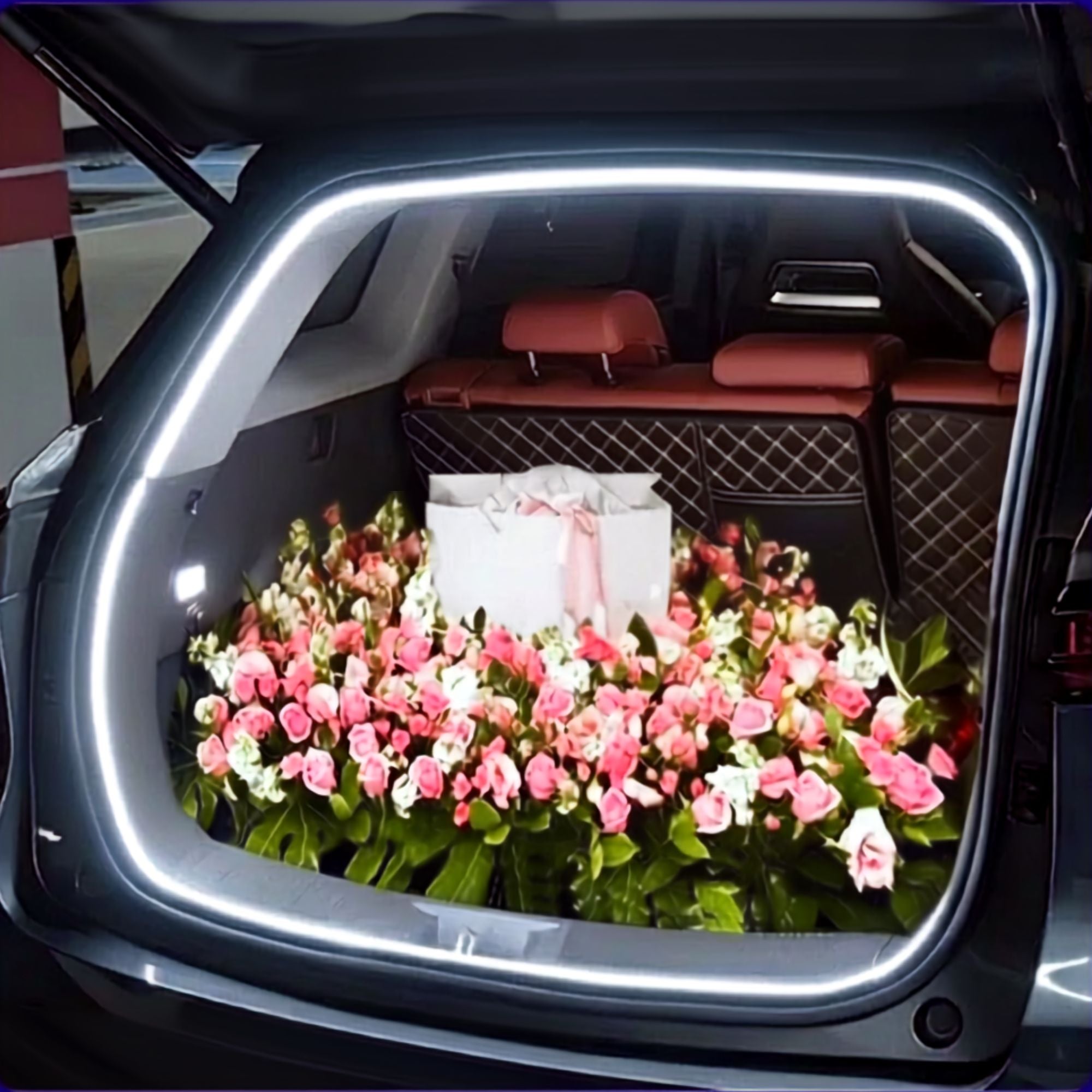 Illuminated LED trunk light strip framing a car boot filled with pink and white rose bouquets at night