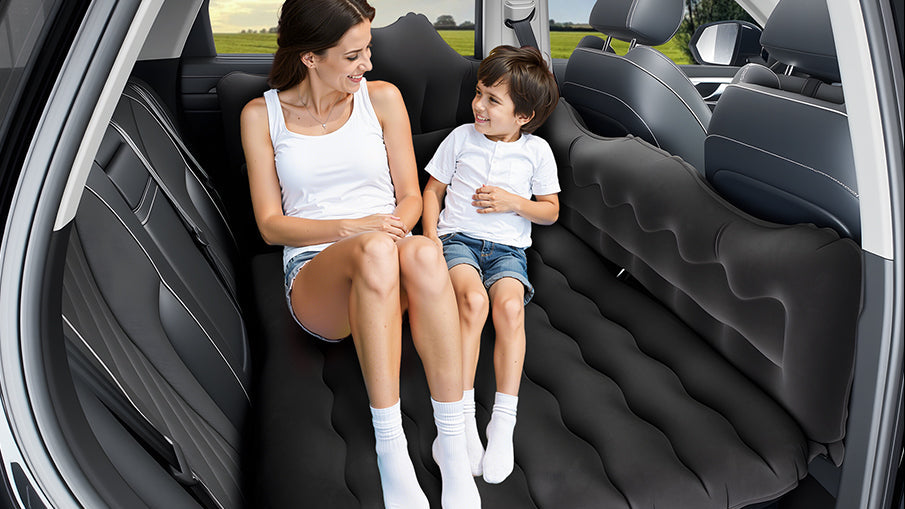 An inflatable car air mattress set up inside a vehicle's back seat, with a woman and child sitting on it. The left side includes text reading 'Universal Car Air Mattress' and small icons showing compatibility with RV, car, MPV, SUV, and minivan.