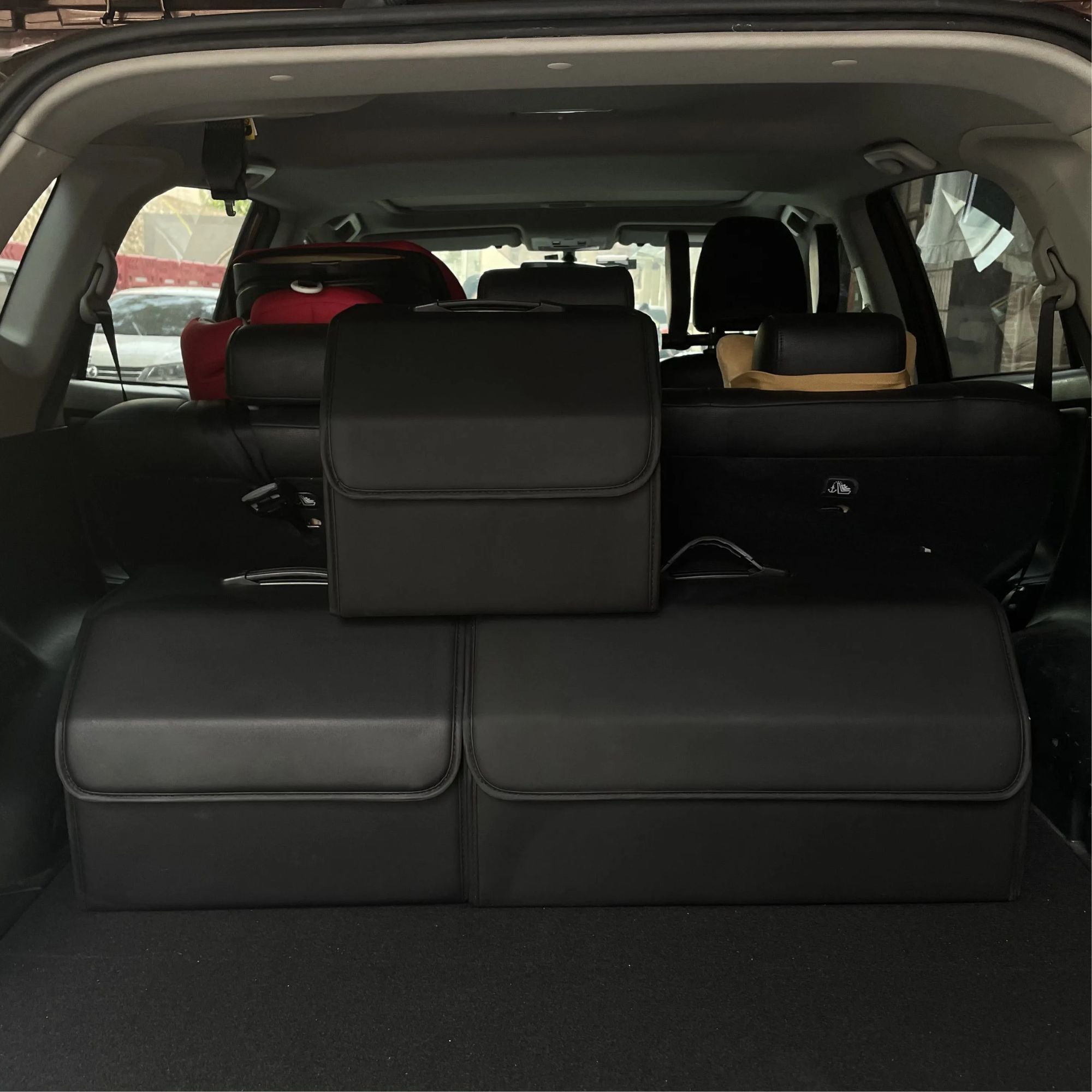 Three different sizes of black leather car boot organisers sitting side-by-side inside the boot of a luxury SUV, demonstrating relative scale.
