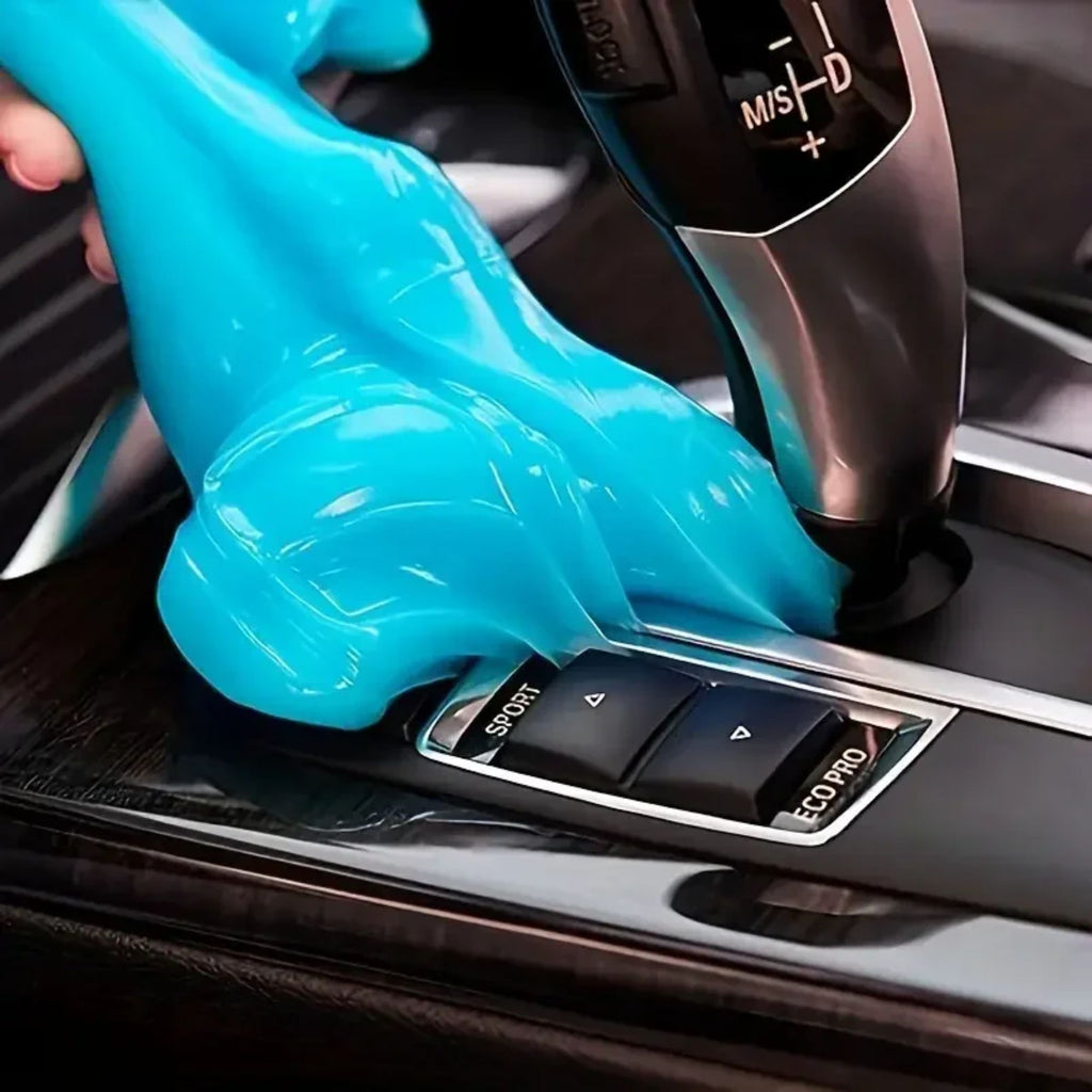 Blue car cleaning putty molded securely over a modern vehicle gear selector and center console buttons to lift dust from tight crevices.