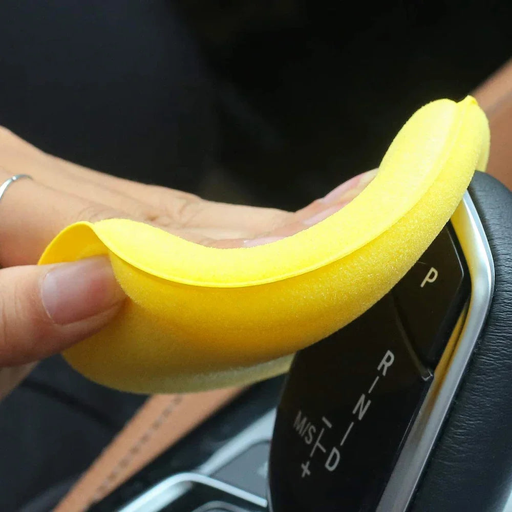 Yellow circular car interior cleaning and waxing sponge pad flexed by hand near a vehicle's central gear shifter.