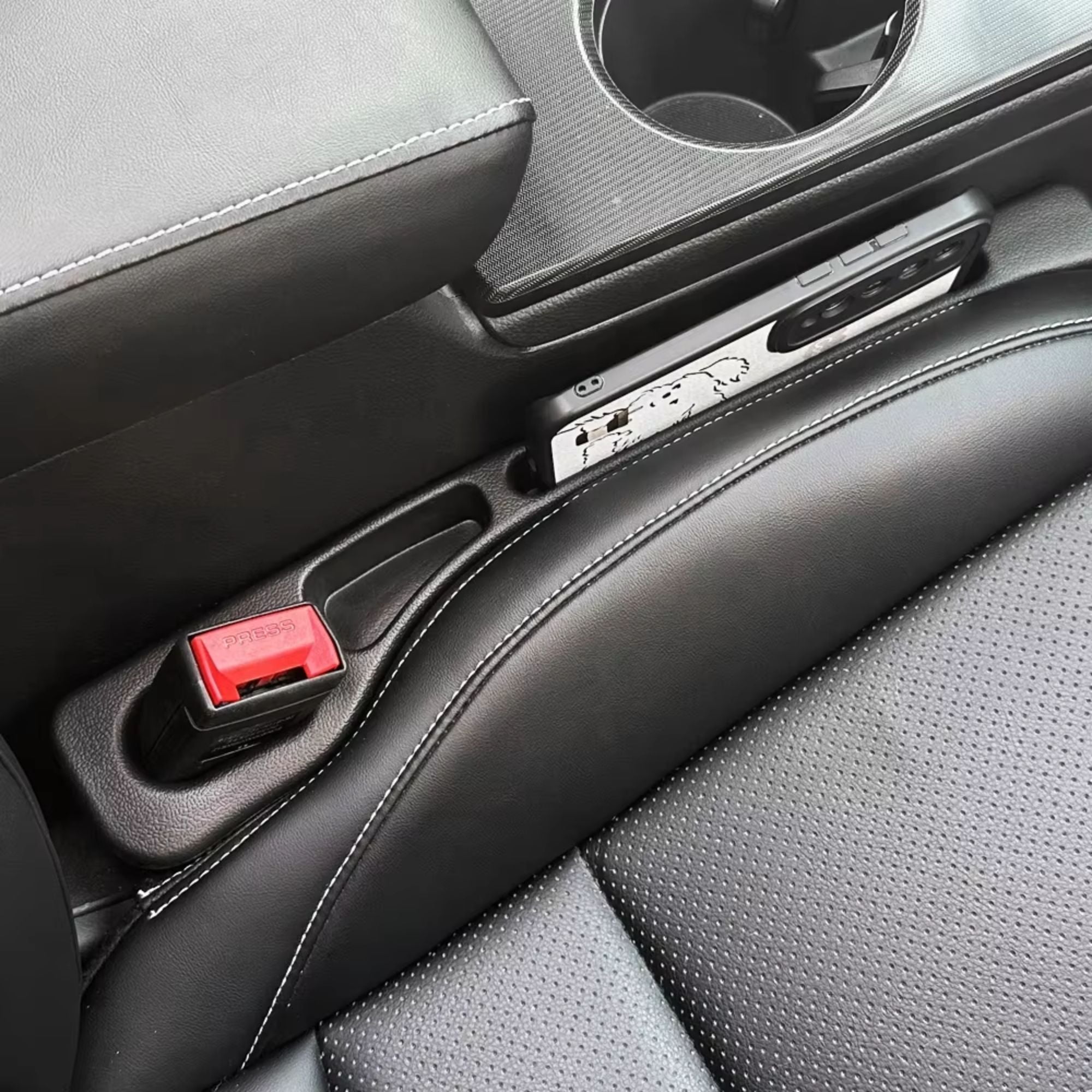 Close-up of a black car seat gap filler installed next to a seatbelt buckle, highlighting the cutout slot for a charging cable.