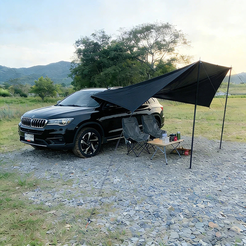Black car side awning attached to a black SUV, providing outdoor shade for a camping table and chairs.