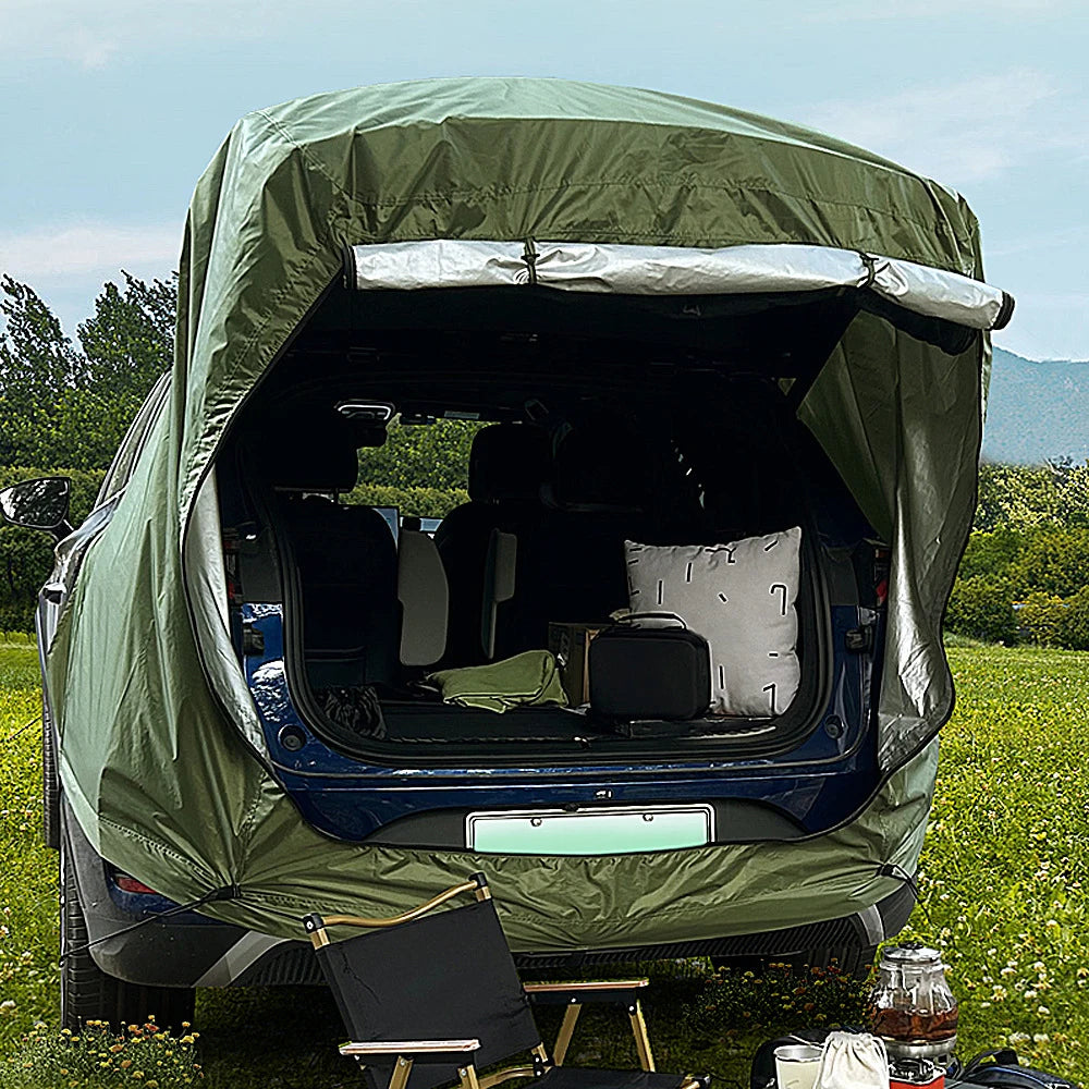 Tactical green car tailgate tent set up in a camping environment, showing the open vehicle boot and expanded rear living space.
