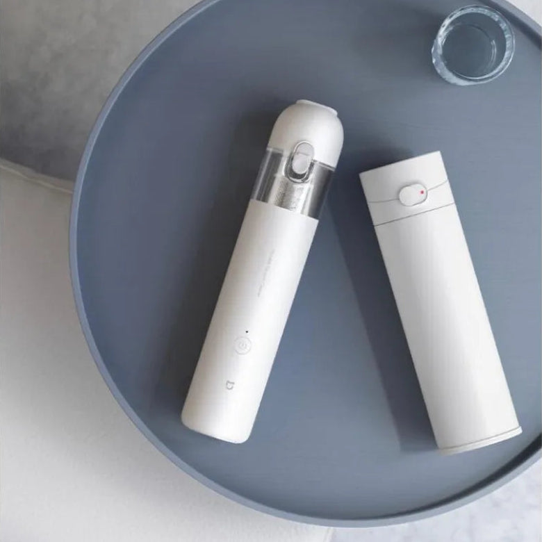 Cordless handheld mini dust collector with its protective white cap removed, resting flat on a circular grey tray.