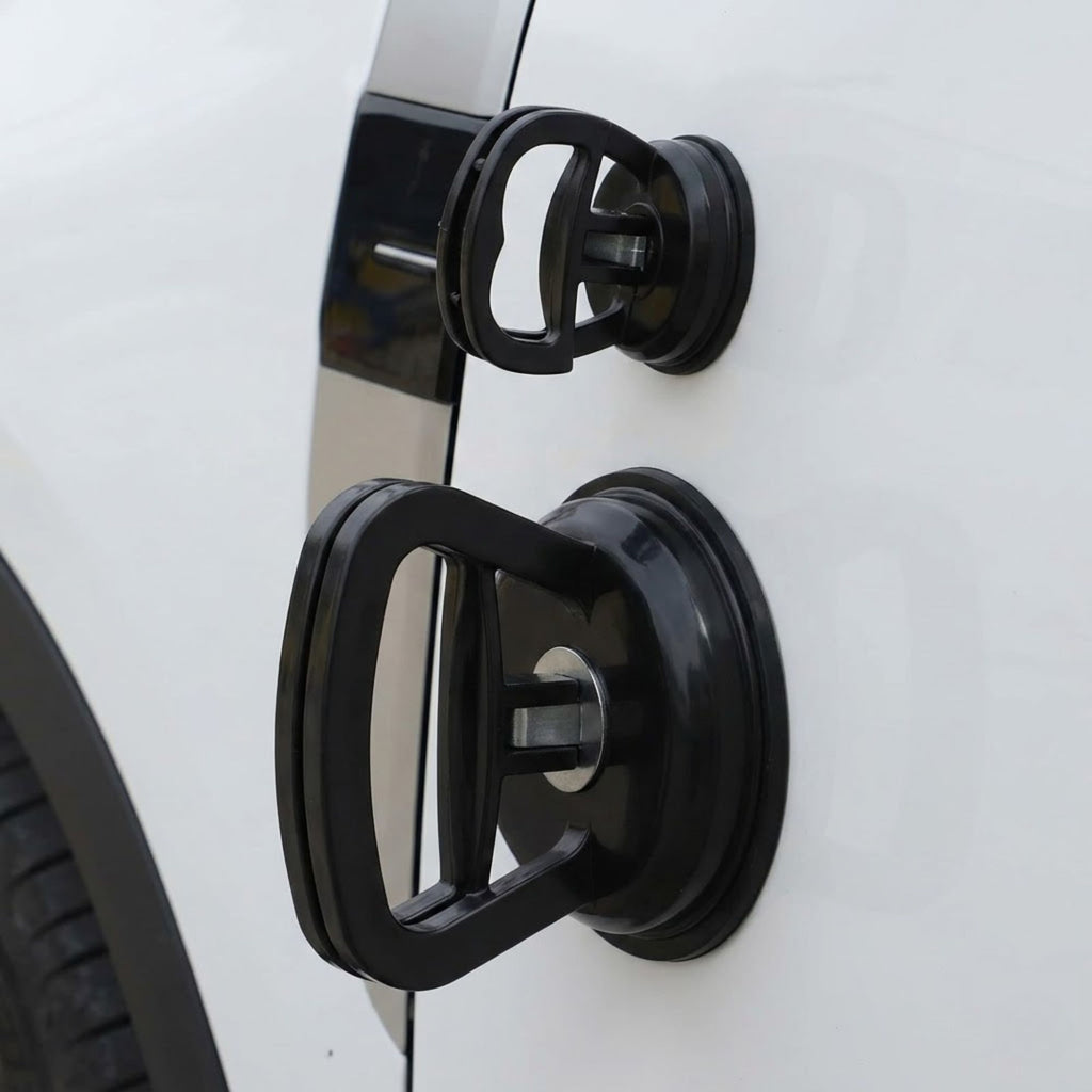 Both large and small black suction cup dent pullers attached simultaneously to the side door panel of a white car to demonstrate scale.