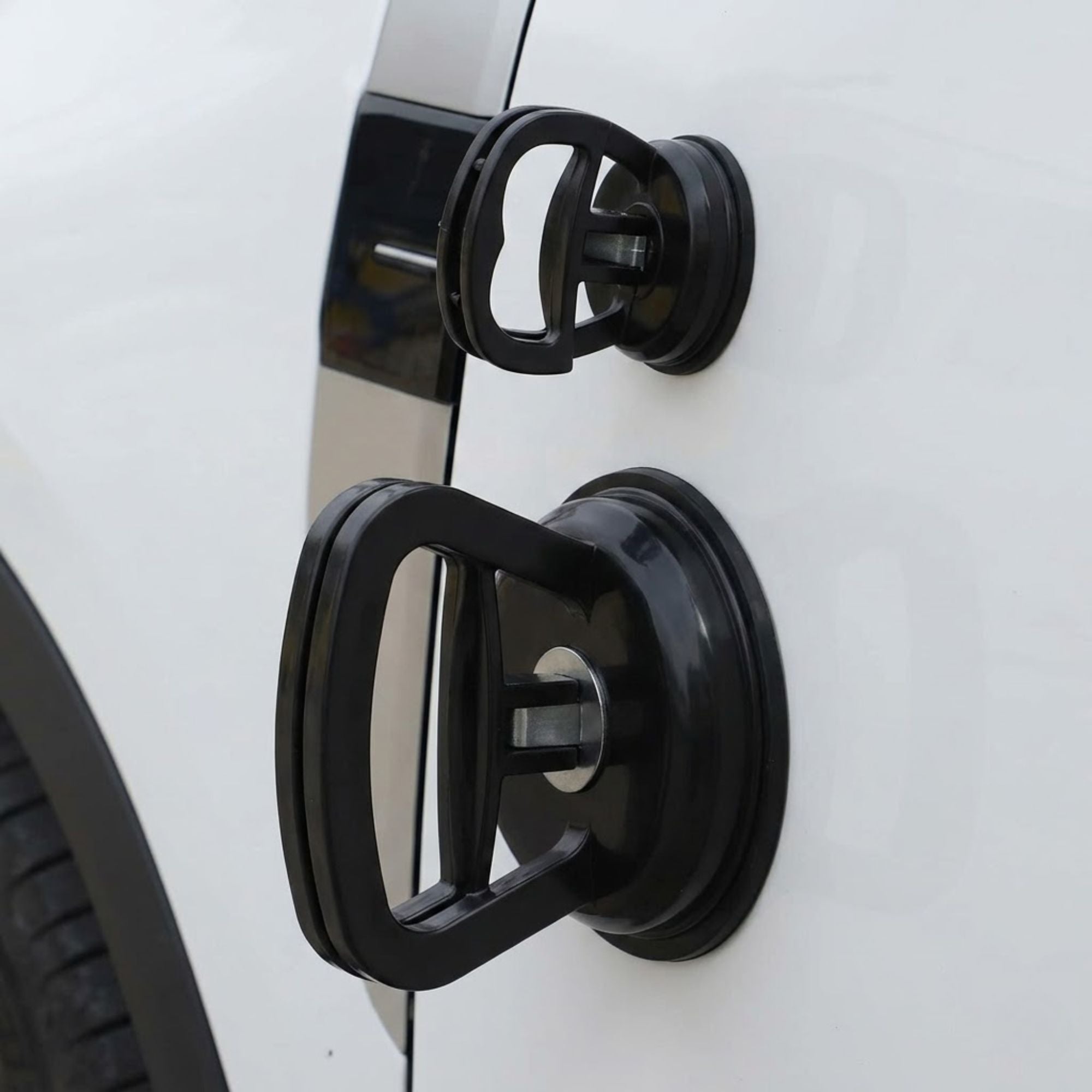 Both large and small black suction cup dent pullers attached simultaneously to the side door panel of a white car to demonstrate scale.
