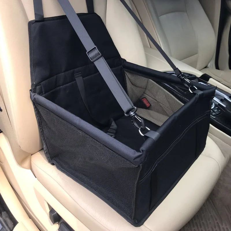 Black folding pet car seat carrier installed empty on a vehicle passenger seat showing the adjustable headrest straps and mesh ventilation.
