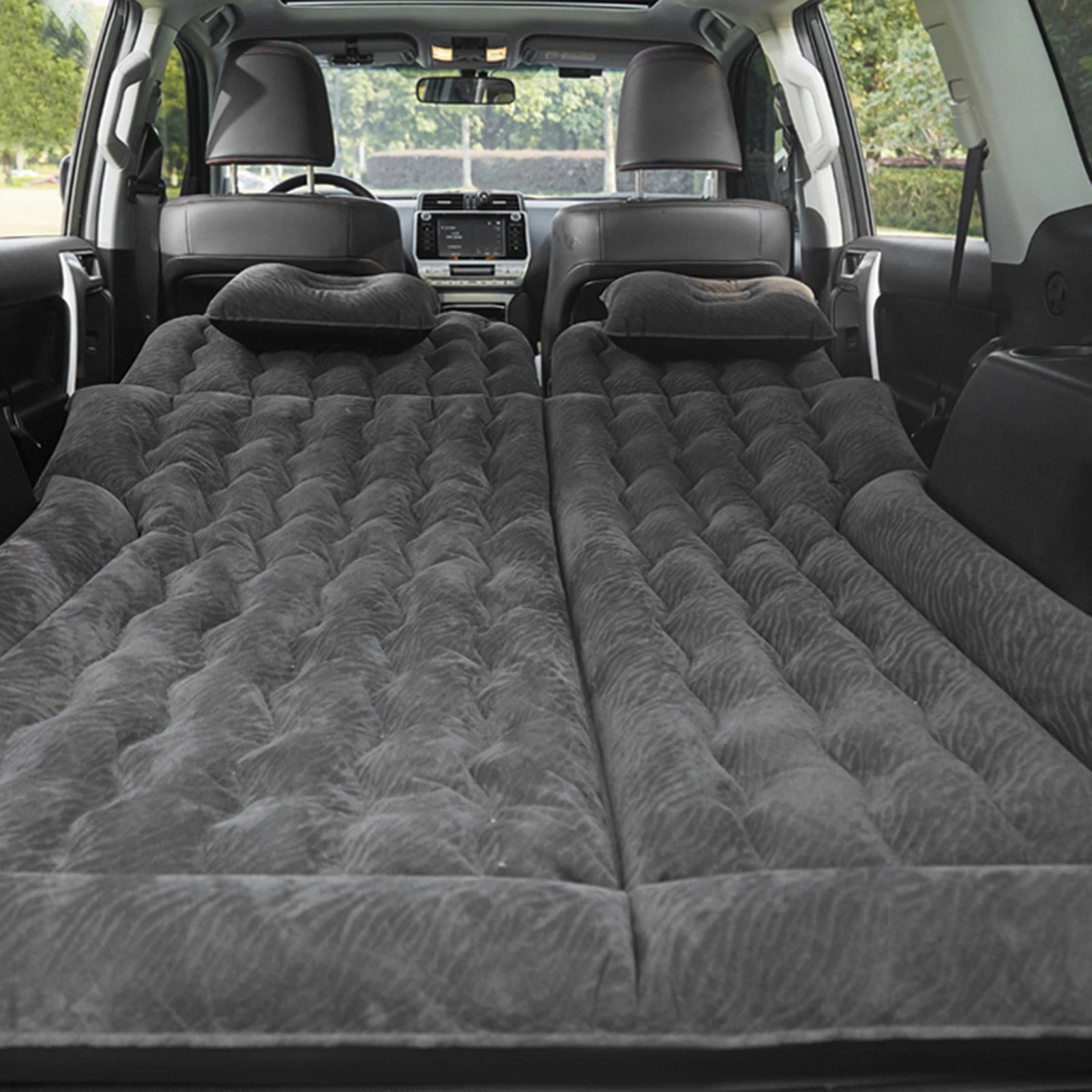 Black inflatable car travel mattress fully deployed in the flat cargo area of an SUV with two headrests positioned at the rear.