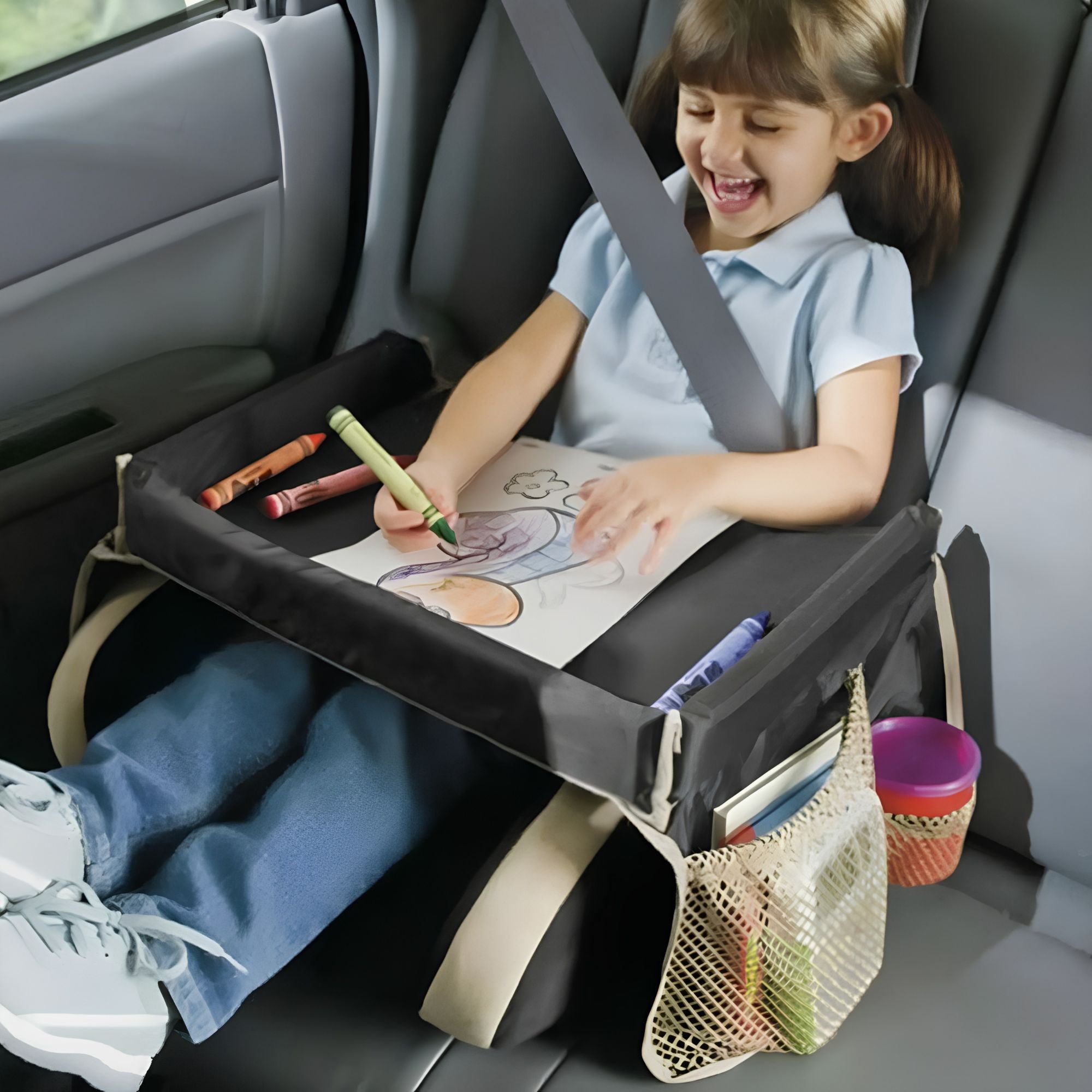 Young girl smiling while colouring on a black kids car seat travel tray secured in the back seat