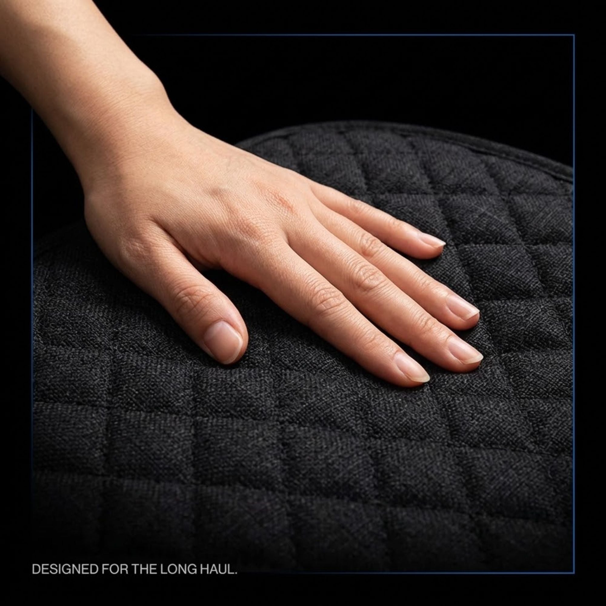 A close-up of a person's hand resting on a black quilted cushion, with the text 'DESIGNED FOR THE LONG HAUL' at the bottom left.