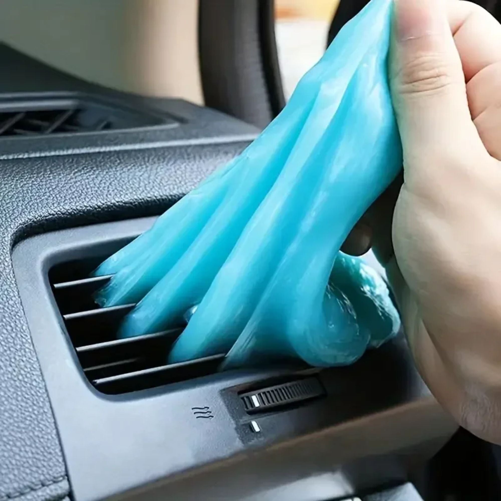Blue reusable car dust remover gel being pressed deep into and pulled out of a vehicle air conditioning vent to extract trapped dirt.