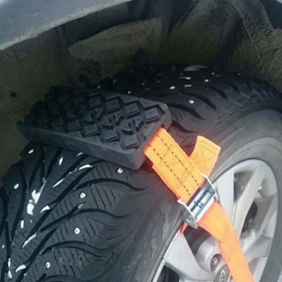 Strap-On Tyre Traction Cleat fastened around a snow-covered tyre with an orange strap and metal buckle