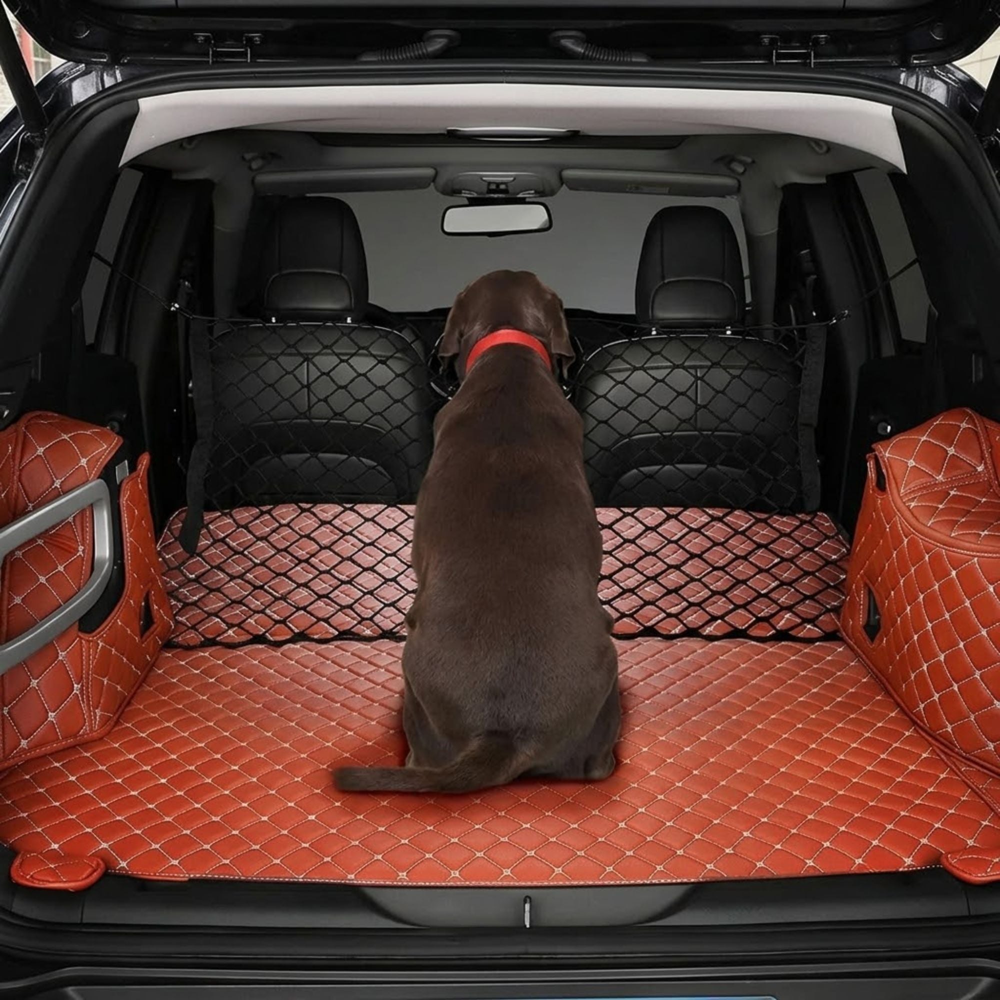 A brown dog sits in the back of an open SUV trunk, facing the rear seats. The cargo area is lined with a quilted orange-brown cargo mat, flanked by matching side pockets, with black mesh seat covers and a black rear window seat cover installed behind the dog.