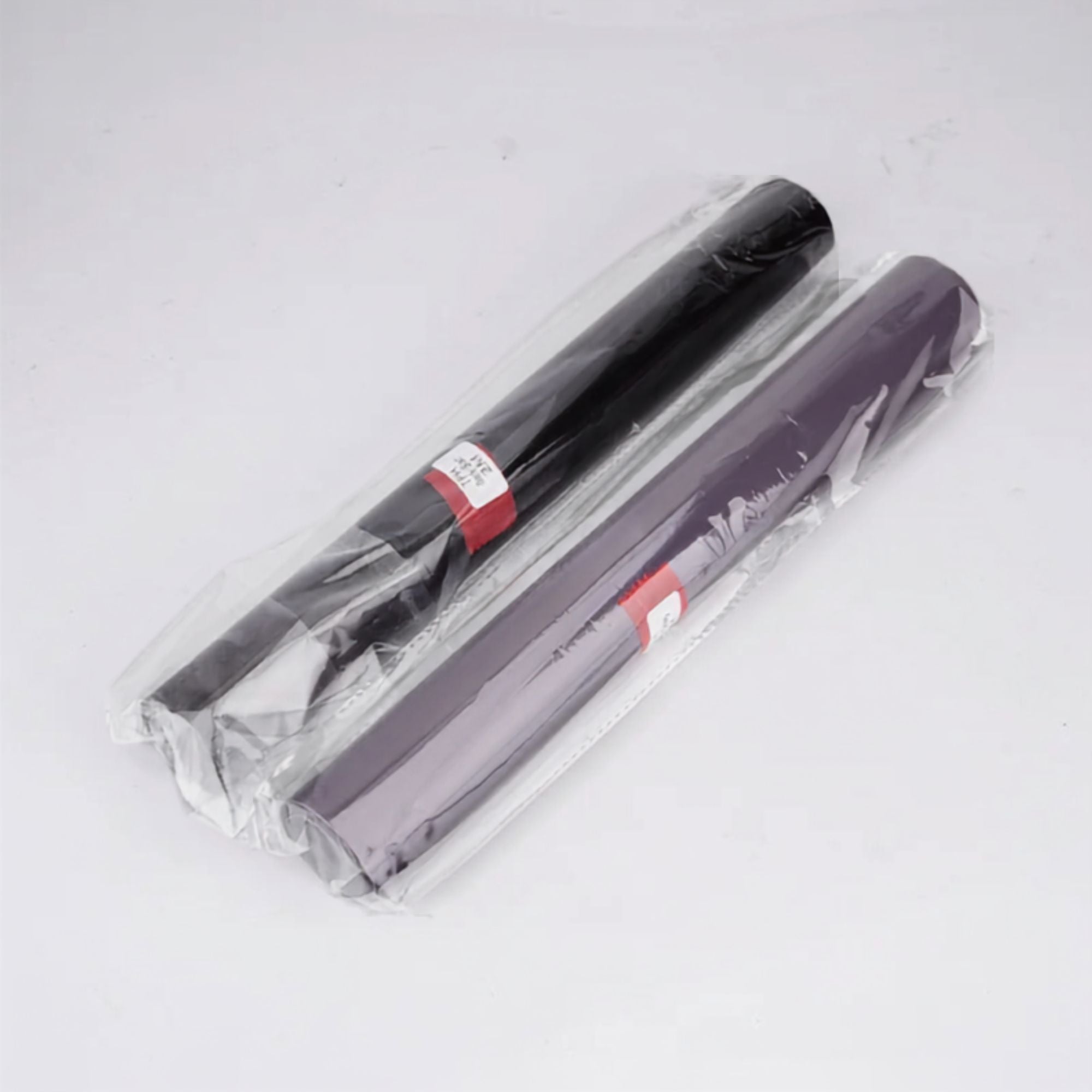 Two rolls of craft vinyl wrap, one black and one dark purple, sealed in clear plastic packaging with red and white labels, on a white background.