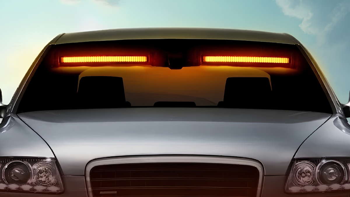 A silver car front grille and hood shown from the front, with two bright amber LED light bars mounted above the windshield against a pale sky background.