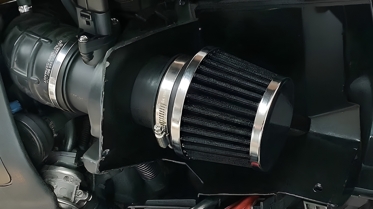 A black cone air filter with silver metal bands, mounted in a black plastic air intake housing within a vehicle engine bay.