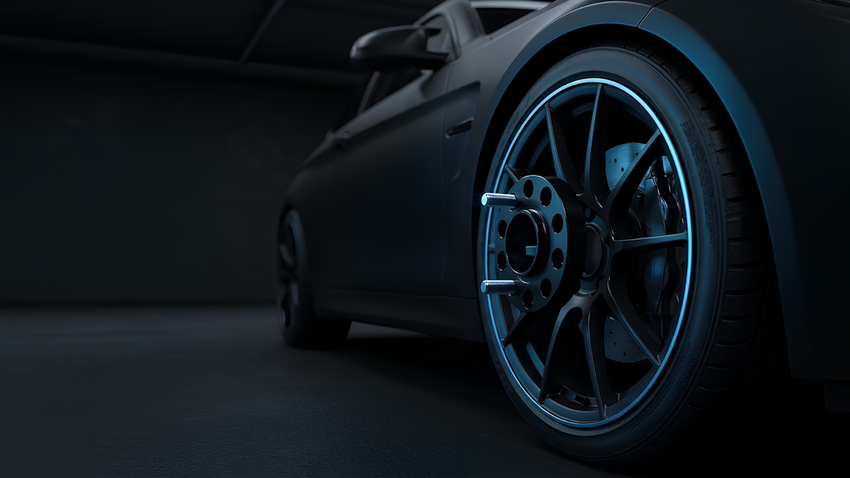 Close-up of a matte black sports car wheel with a dark multi-spoke alloy rim and blue accent lighting, set in a dark studio environment.