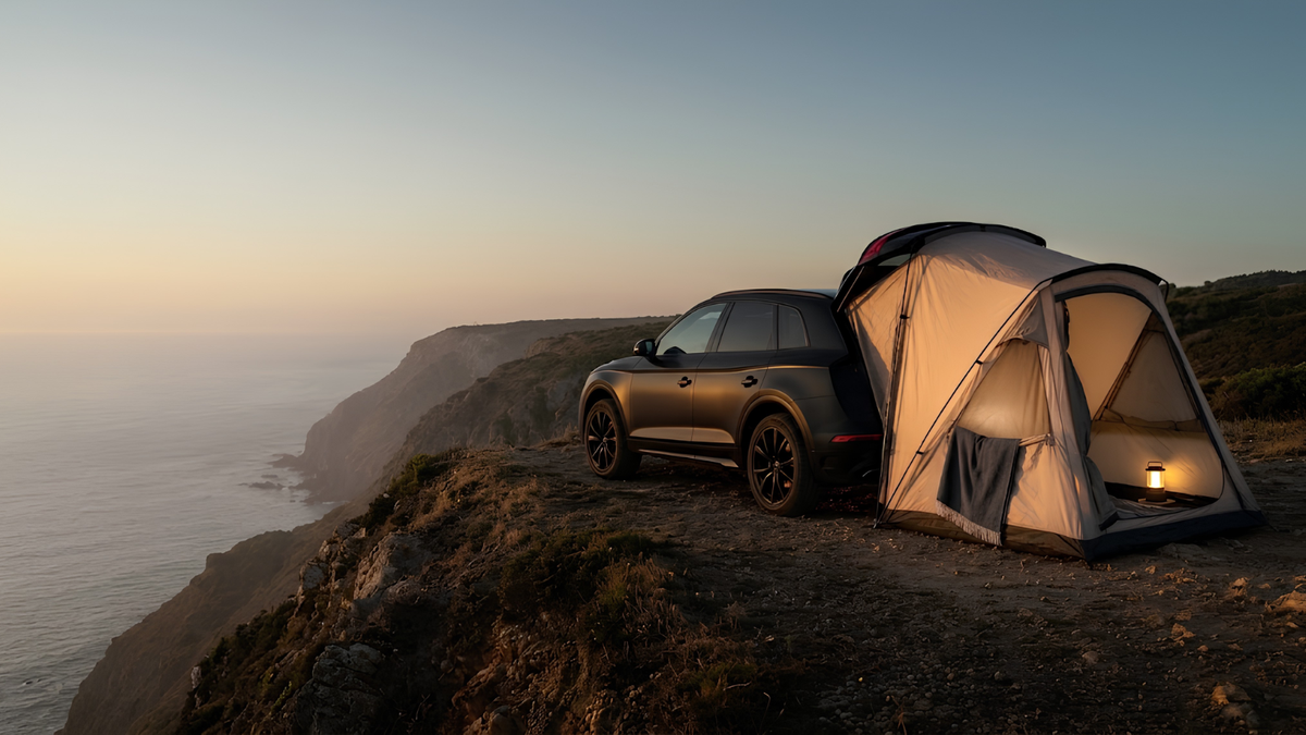 A dark SUV parked beside a lit camping tent on a cliffside path at sunset, with ocean and coastline visible in the background.