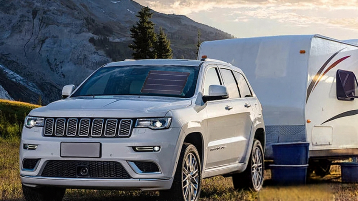 A white Jeep Grand Cherokee SUV parked outdoors in a grassy field with mountains and trees in the background, towing a white travel trailer.
