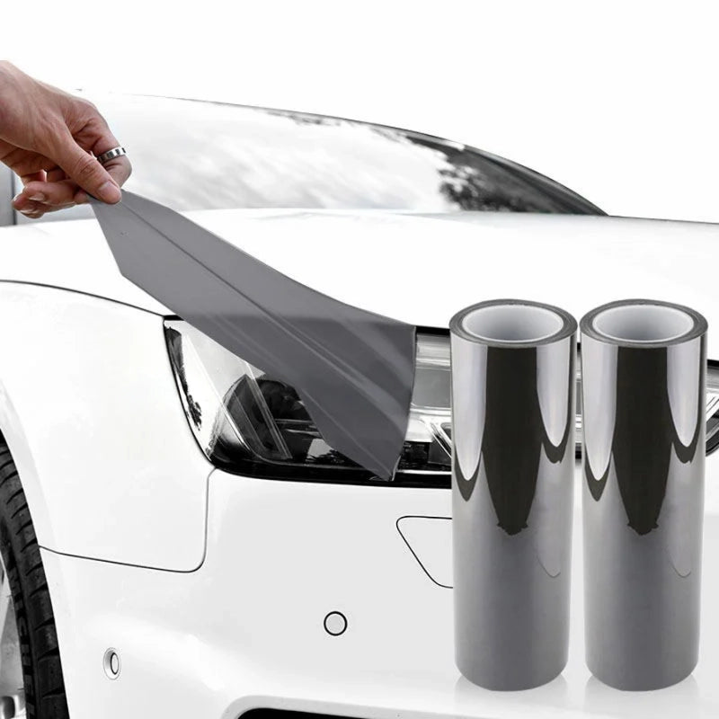 Person applying car wrap film to a white car with two rolls of car wrap in the foreground.