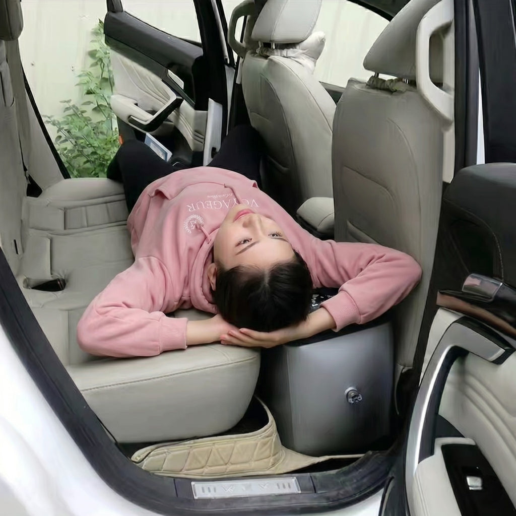 A woman lying down comfortably in the back seat of a vehicle, utilising the black inflatable bed extender to create a flat, supportive sleeping surface over the rear footwell.